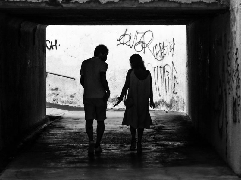 Two people walking side by side through a tunnel, seen in silhouette