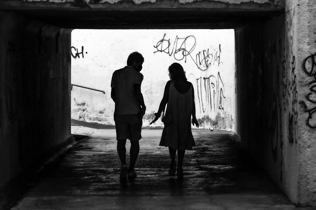 Two people walking side by side through a tunnel, seen in silhouette