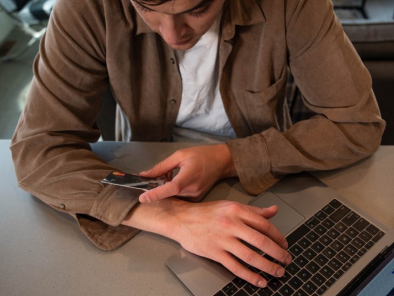 A person holding a payment card while using a laptop