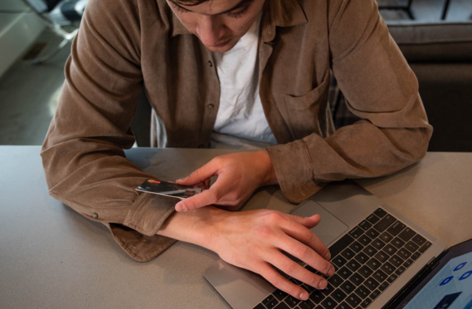 A person holding a payment card while using a laptop