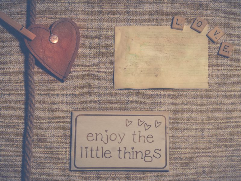 A wooden heart, letter tiles spelling love and a card reading enjoy the little things on burlap