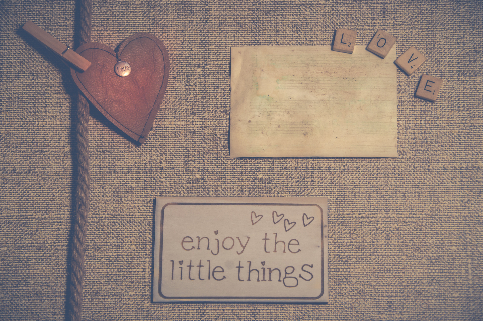 A wooden heart, letter tiles spelling love and a card reading enjoy the little things on burlap