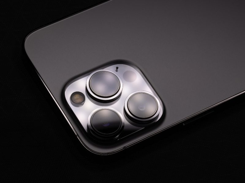 The back of a smartphone with three camera lenses on a dark surface