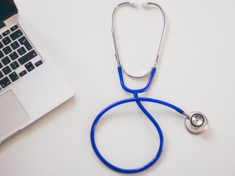 A blue stethoscope next to a laptop on a white desk