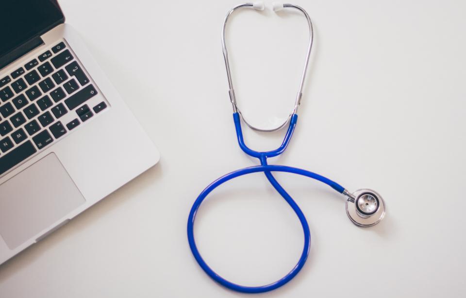 A blue stethoscope next to a laptop on a white desk